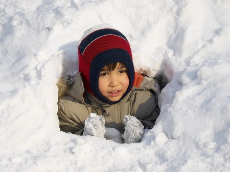 Funny little boy playing in snow, outdoors in winter.