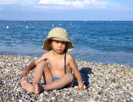 Small boy sit on the beach with hat.の写真素材