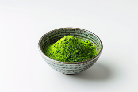 A bowl of vibrant green matcha powder on a white surfaceの素材