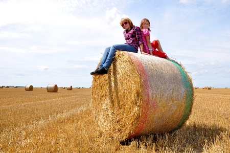 girls sitting on a bale of strawの写真素材