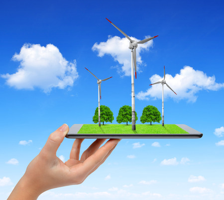 Hand holding digital tablet with a wind turbines and trees . Green energy concept.の写真素材