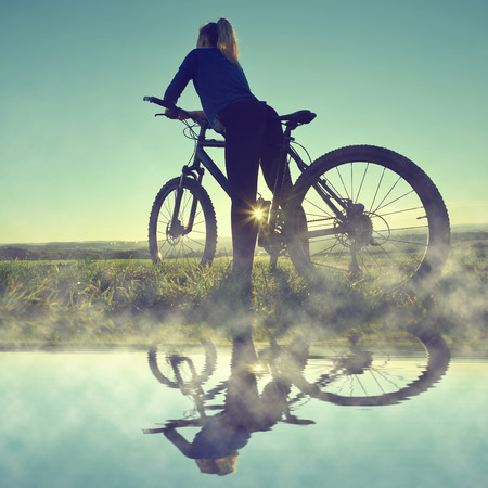 Girl on a bicycle in the sunset reflected on the water surfaceの写真素材