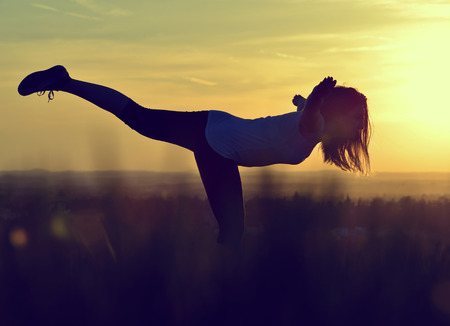 Silhouette of young woman stretching on a meadow at sunsetの写真素材
