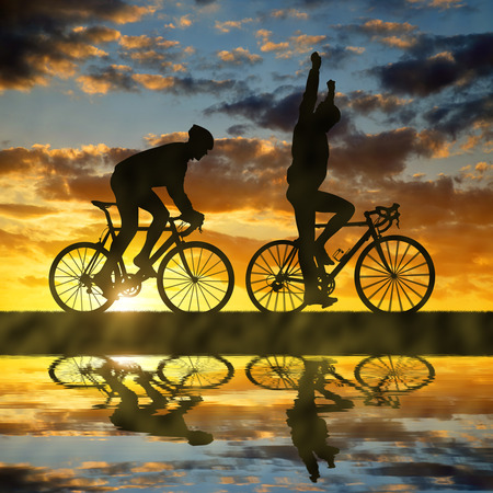 silhouette of two cyclists riding a road bike at sunsetの写真素材
