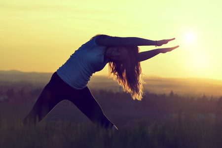 Silhouette of young woman stretching on a meadow at sunsetの写真素材