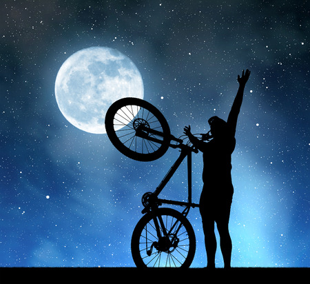 Silhouette of a man with a bicycle in the night sky with the moon.の写真素材