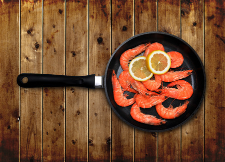 Skillet with shrimp and lemon on wooden board.の写真素材