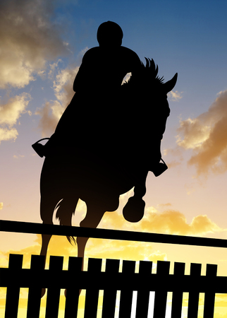 Silhouette of a rider on a horse jumping over obstacle at sunset.の写真素材