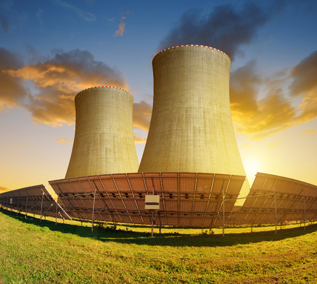 Solar energy panels and nuclear power plant at sunset.