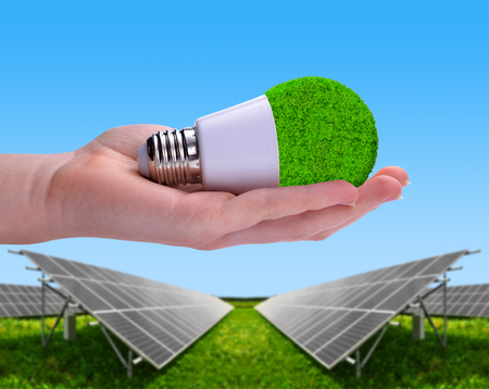 Eco LED bulb in hand in the background solar energy panels. The concept of sustainable resources.の写真素材