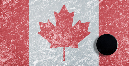 Black hockey puck on ice rink with Canadian flag.の写真素材