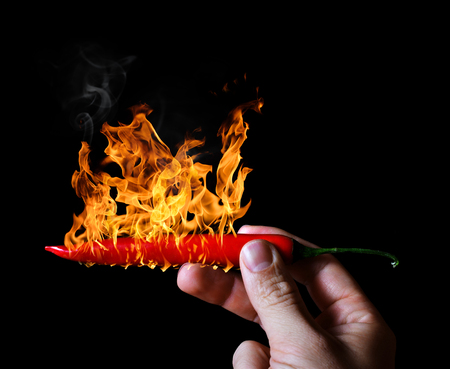 Hand holding burning red hot chili peppers on black background.の写真素材