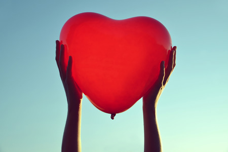 Hands holding red balloon in the shape of heart at sunset.の写真素材