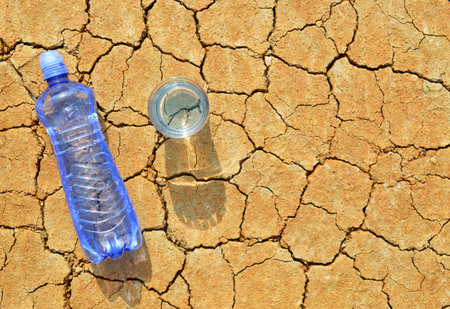 Bottle and glass of water on dry cracked soil. Concept of global warming.