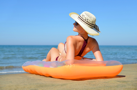 Caucasian girl with hat lying on inflatable mattress on the beach. Summer vacation by the sea.の写真素材