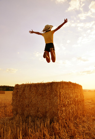 Girl jumping on a straw bale at sunset.の写真素材