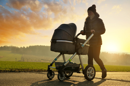 Walking woman with baby stroller at sunset.の写真素材