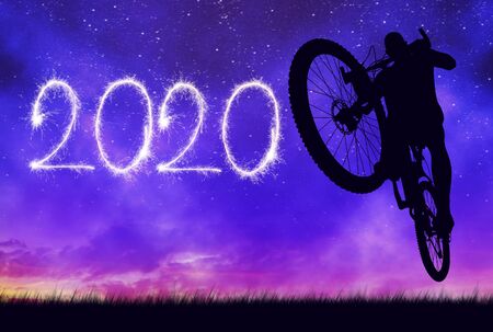 Forward to the New Year 2020. Cyclist jumping on bicycle with night sky at the background.の写真素材