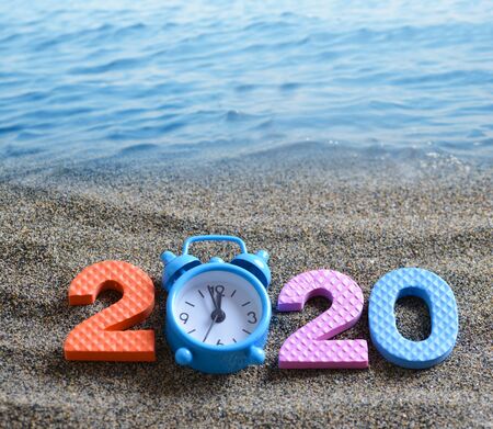 Number 2020 and alarm clock on the sand beach. Happy New Year.の写真素材