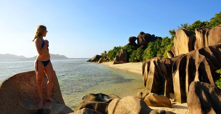 Woman looks at the beach Anse Source d'Argent with big granite rocks at sunset. La Digue Island, Indian Ocean, Seyshelles. Vacations concept.の写真素材