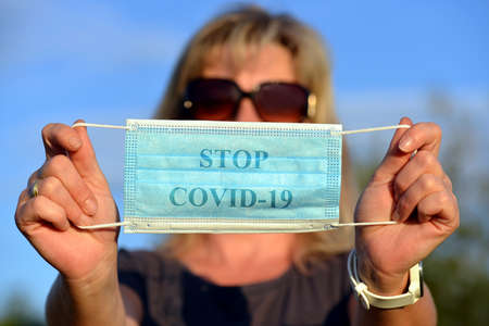 Woman holding a blue protective medical mask in her hand with stop covid 19 text.の写真素材