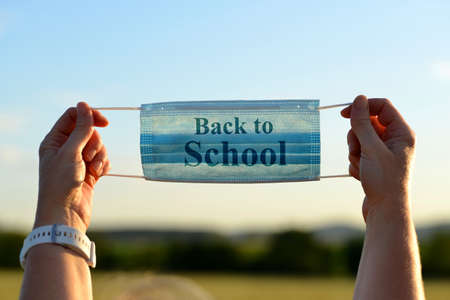 Female hands holding protective medical mask with Back to School text. Covid-19 pandemic theme.
