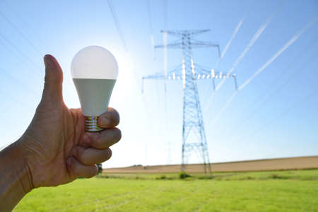 Hand with thumb up holding eco LED light bulb with transmission tower at the background. Energy saving concept.の写真素材