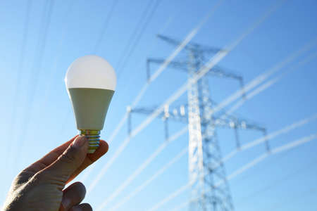 Hand holding eco LED light bulb with transmission tower at the background. Energy saving concept.
