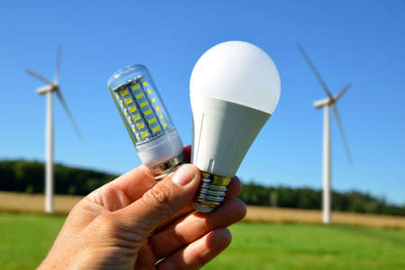 Hand holding eco LED light bulbs, at the background wind turbines on meadow. Energy saving lamps.の写真素材