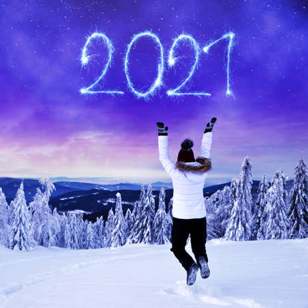 Woman jumps in a snowy winter landscape. 2021 writen with sparklers on night sky. New Year card.の写真素材