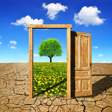 Dry country with cracked soil and open wooden door to the beautiful spring landscape with blooming meadow and tree. Climate change concept.の写真素材