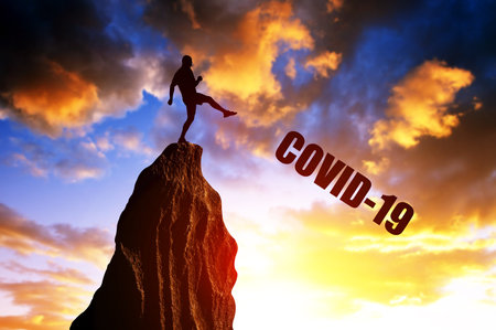 Man kick from the rock the text covid-19 in the sunset. End of Covid-19 pandemic concept.の写真素材