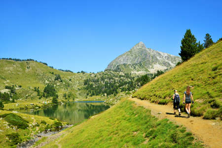 Hikers on a trip in Neouvielle national nature reserve, Lac du Milieu, French Pyrenees. Beautiful summer mountain landscape in the sunny day.の写真素材