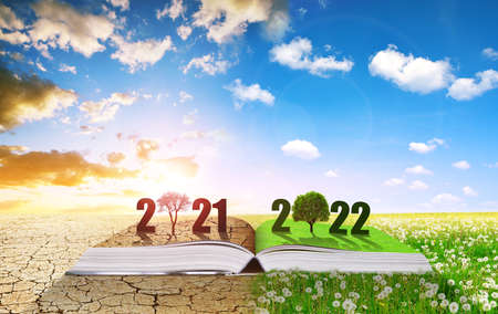 Open book with number 2021 and 2022. Dry country with cracked soil and spring meadow in sunny day. Concept of Happy New Year. Global warming or climate change theme.の写真素材