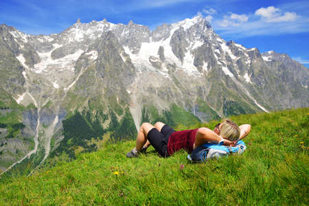 Tourist lying on a meadow in sunny day, at the background mount Grandes Jorasses, Aosta valley, Italy.の写真素材
