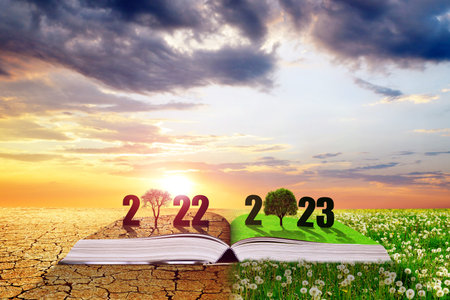 Open book with numbers 2022 and 2023 at sunset. Dry country with cracked soil and spring meadow with dandelions. Concept of Happy New Year. Global warming or climate change theme.の写真素材