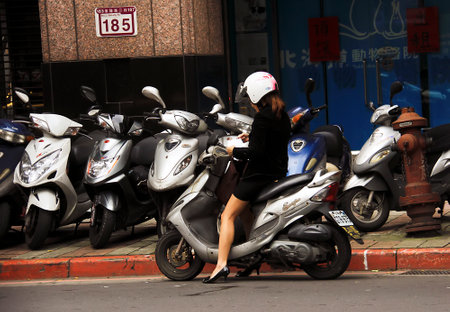 Businesswoman riding a scooter on the streets of Taipei.のeditorial素材