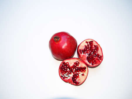 christmas decoration background for greeting card, red pomegranate fruit, whole fruit and sliced in half, red pomegranates in detail, close-up, white backgroundの写真素材
