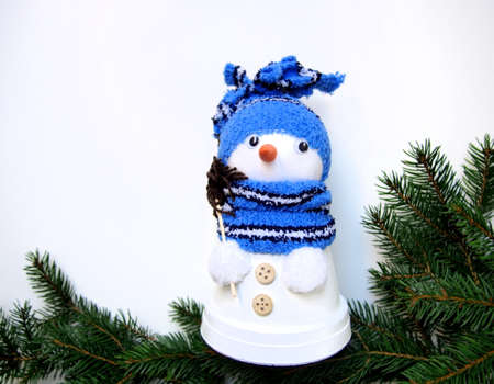 christmas decoration background for greeting card, spruce twigs with white snowman made of flowerpots with blue scarf and hat and red nose made of carrot, white backgroundの写真素材
