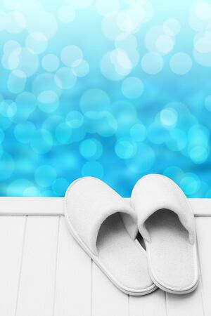 Pair of white hotel, spa, wellness, slippers on pier with bokeh background with space for textの写真素材