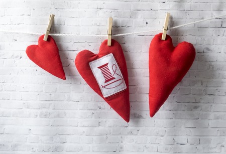 Three textile red hearts weigh on a rope, on clothespins. White brick background. Place for text. Wedding concept, mother's day.の写真素材