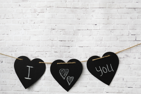 Greeting card Valentine. Three hearts hang on a rope, on a brick light wall. The composition of the inscription for Valentine's Day or for the wedding - I love you.の写真素材