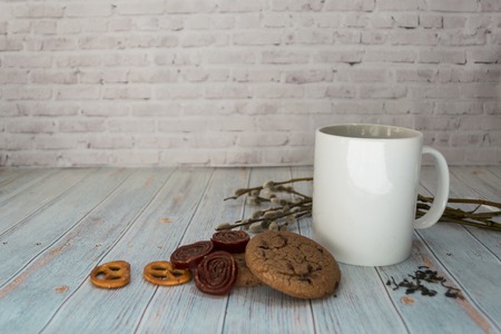White mug of tea, oatmeal cookies and sweets, with a willow branch on a light wooden background. Concept Easter and Palm Sunday.の写真素材