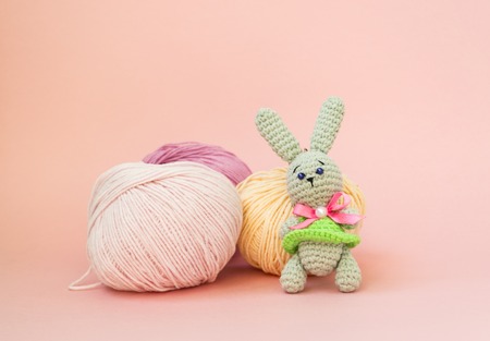 Gray knitted hare stands on the background of multi-colored balls of yarn on a pink background. There is a place for text. The concept of hobby, needlework.の写真素材