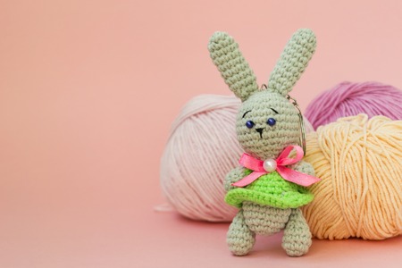 Gray knitted hare stands on the background of multi-colored balls of yarn on a pink background. There is a place for text. The concept of hobby, needlework.の写真素材