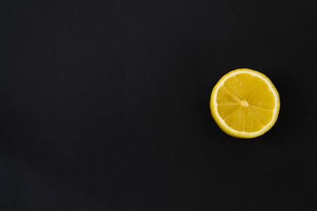 Round slice of yellow lemon, on a black background. There is a place of text.の写真素材