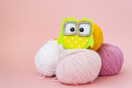 Self-made soft toy owl made of felt, on a color monophonic background. The owl stands next to the balls of yarn. There is a place for text. Hobby conceptの写真素材