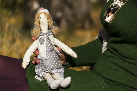 Female tilde doll in a multi-colored dress sitting on a female hand. Registration of holidays. Interior fairy doll handmade. Art and creativity.の写真素材