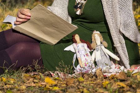 Two female tilde dolls in multi-colored dresses are sitting on the grass near the girl who is reading a thick book. Registration of holidays. Interior fairy doll handmade. Art and creativity.の写真素材