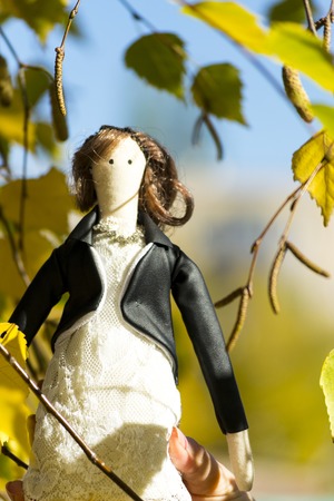 A female Tilda doll in a colorful dress looks out from behind a tree. Registration of holidays. Interior fairy doll handmade. Art and creativity. Blurred background, there is a place for text.の写真素材